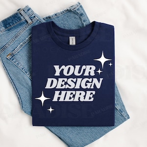 May include: A navy blue t-shirt with the text "YOUR DESIGN HERE" in white. The shirt is folded and placed on top of a pair of blue jeans.