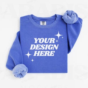 May include: A blue sweatshirt with the text "YOUR DESIGN HERE" in white. The sweatshirt has a crew neck and long sleeves. There are white stars on the sweatshirt.