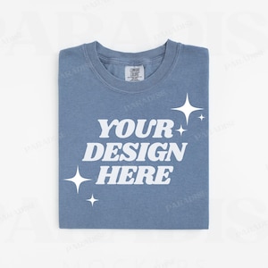 Peut inclure: Un t-shirt bleu avec le texte "YOUR DESIGN HERE" en blanc. Le t-shirt a un aspect vieilli et est décoré d'étoiles blanches.