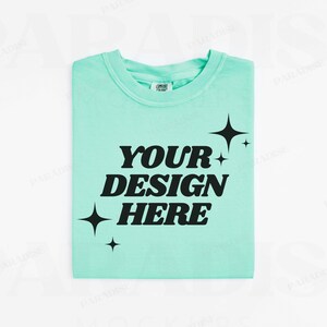 May include: A light blue t-shirt with the text "YOUR DESIGN HERE" in black. The text is in a retro font style and is surrounded by small black stars.