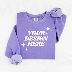 May include: A purple sweatshirt with the text "YOUR DESIGN HERE" in white. The sweatshirt has a crew neck and long sleeves. There are small white stars scattered around the text.
