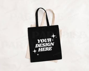 May include: Black tote bag with white text that says "Your Design Here" and stars. The bag is sitting on top of a cream colored tote bag.