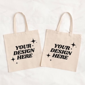 May include: Two white canvas tote bags with black handles. Both bags have the text "YOUR DESIGN HERE" printed in a retro font with small stars around the text.