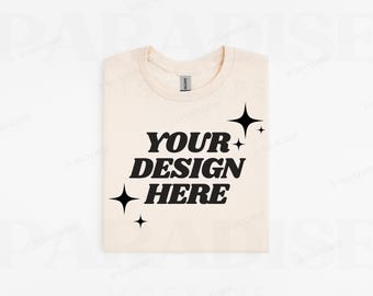 Puede incluir: Una camiseta beige con el texto "YOUR DESIGN HERE" en negro, rodeada de pequeñas estrellas negras.