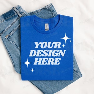 May include: A folded royal blue t-shirt with the text "YOUR DESIGN HERE" in white. The t-shirt is folded on top of a pair of blue jeans.