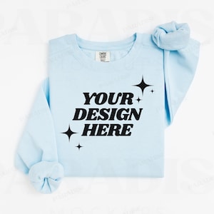 May include: A light blue sweatshirt with the text "YOUR DESIGN HERE" in black lettering and small star designs.