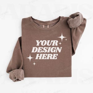 May include: A brown sweatshirt with the text "YOUR DESIGN HERE" in white. The sweatshirt has a crew neck and is folded in half. There are small white stars on the sweatshirt.