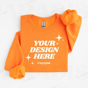 以下が含まれることがあります： 白い「YOUR DESIGN HERE」の文字と星のグラフィックが入った、鮮やかなオレンジ色のスウェットシャツ。袖は折り返されています。スウェットシャツはGildanブランドです。「PARADISE MOCKUPS」の文字が下にあります。