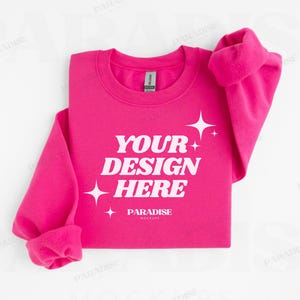 Op de afbeelding: Een felroze sweatshirt met de tekst "YOUR DESIGN HERE" in het wit, samen met sterren. De mouwen zijn opgerold en het Gildan-label is zichtbaar. Dit is een mock-up.