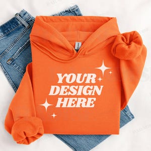 Könnte beinhalten: Orangefarbener Hoodie mit einem weißen Aufdruck, der "YOUR DESIGN HERE" und weiße Sterne zeigt.