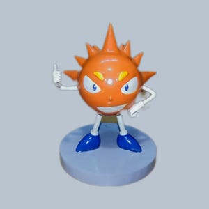 Puede incluir: Figurita de personaje de dibujos animados naranja y azul con una cabeza puntiaguda y una cara sonriente. La figurita está de pie sobre una base azul.