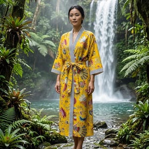 Puede incluir: Una bata de color amarillo brillante con un estampado colorido de flores y pájaros, mangas largas y un cinturón para anudar. La prenda presenta un ribete a rayas blancas y negras en contraste a lo largo de la abertura frontal y los puños.