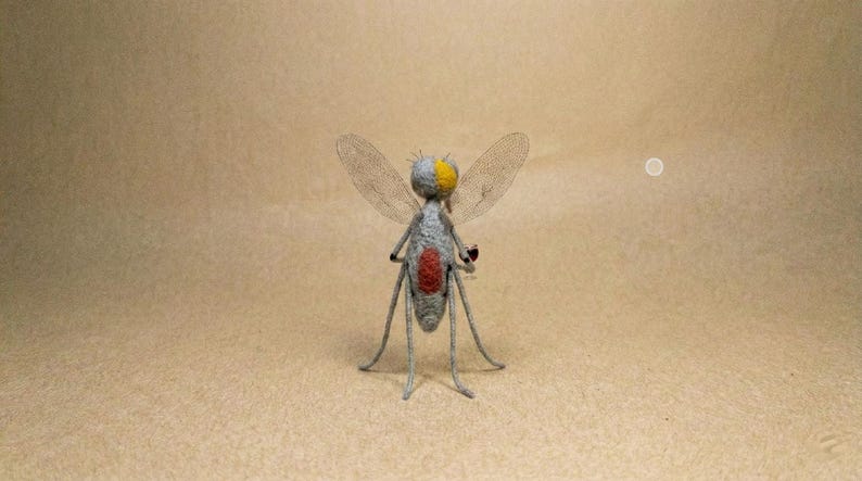 Puede incluir: Una escultura de insecto hecha a mano con cuerpo gris, cabeza amarilla y abdomen rojo. El insecto tiene alas delicadas y transparentes y patas delgadas, sobre un fondo neutro.