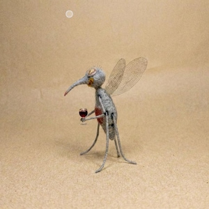 Puede incluir: Una escultura caprichosa de un mosquito sosteniendo un vaso de l&iacute;quido rojo. El mosquito es gris con alas delicadas y una larga prob&oacute;scide. La escultura est&aacute; sobre un fondo neutro.