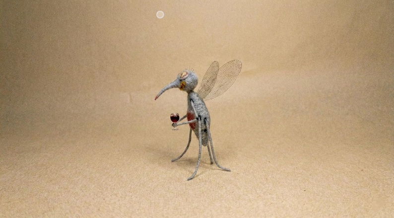 Puede incluir: Una escultura caprichosa de un mosquito sosteniendo un vaso de l&iacute;quido rojo. El mosquito es gris con alas delicadas y una larga prob&oacute;scide. La escultura est&aacute; sobre un fondo neutro.