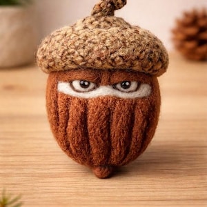 May include: A handcrafted acorn figure with a ninja-like design. The acorn has a brown body and a knitted cap. The eyes are visible through a white mask. The figure is set on a wooden surface.