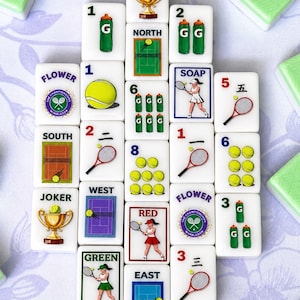 May include: A collection of white Mahjong tiles with tennis-themed illustrations and green accents. The tiles feature tennis balls, rackets, court scenes, and the Wimbledon logo. Green and white tiles are scattered around the main set.