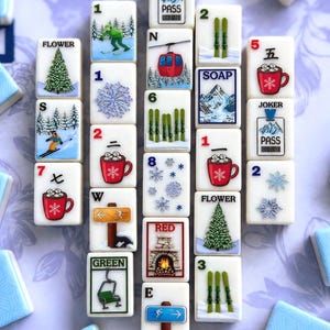Può includere: Una collezione di tessere bianche con illustrazioni a tema invernale e numeri. Le tessere presentano immagini di sciatori, fiocchi di neve, seggiovie e tazze di cioccolata calda. Alcune tessere hanno le parole "JOKER", "PASS", "SOAP", "RED", "GREEN" e "FLOWER".
