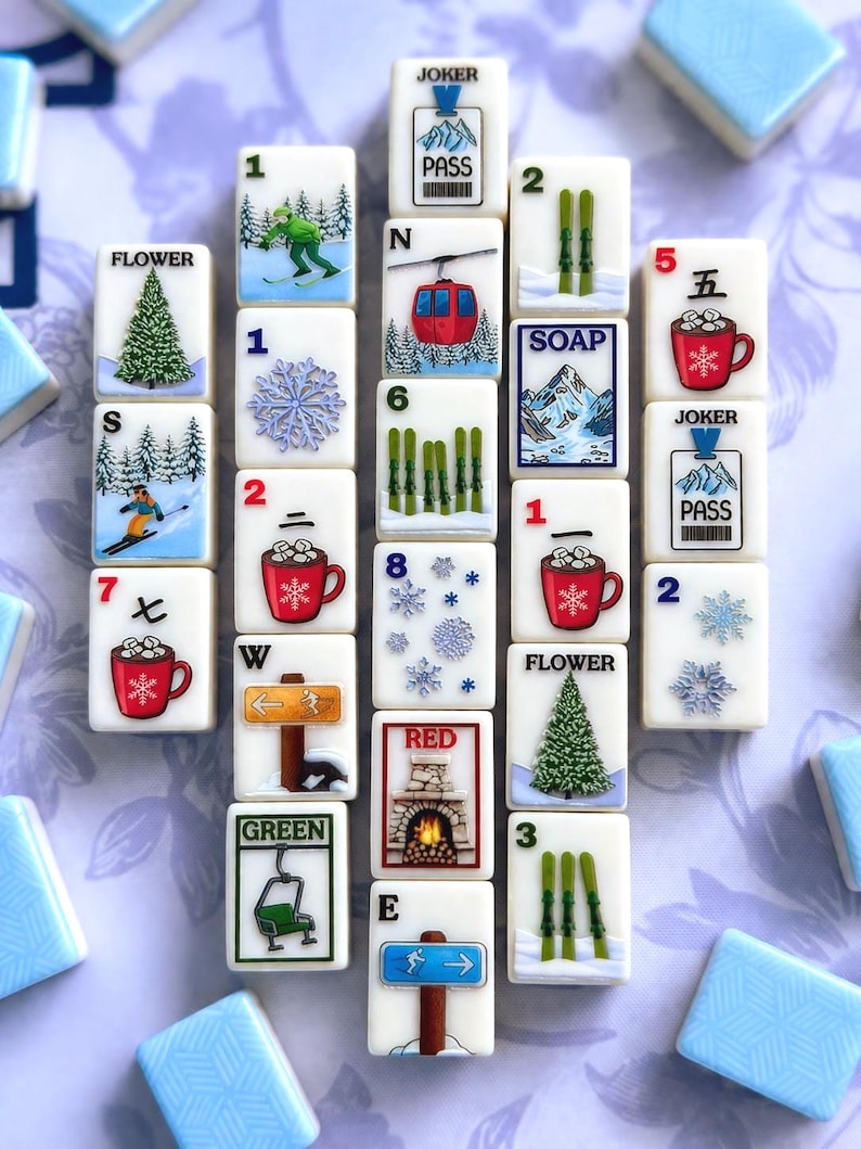 May include: A collection of white tiles with winter-themed illustrations and numbers. The tiles feature images of skiers, snowflakes, ski lifts, and mugs of hot cocoa. Some tiles have the words "JOKER", "PASS", "SOAP", "RED", "GREEN", and "FLOWER".