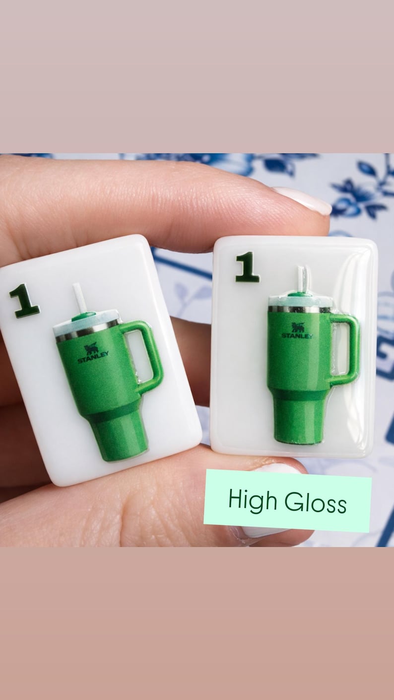 Puede incluir: Dos baldosas rectangulares blancas con un dise&ntilde;o de vaso Stanley verde. Cada baldosa tiene el n&uacute;mero "1" en la esquina superior izquierda. El vaso es verde con un asa y una pajita blanca. El texto "High Gloss" est&aacute; en un rect&aacute;ngulo verde.