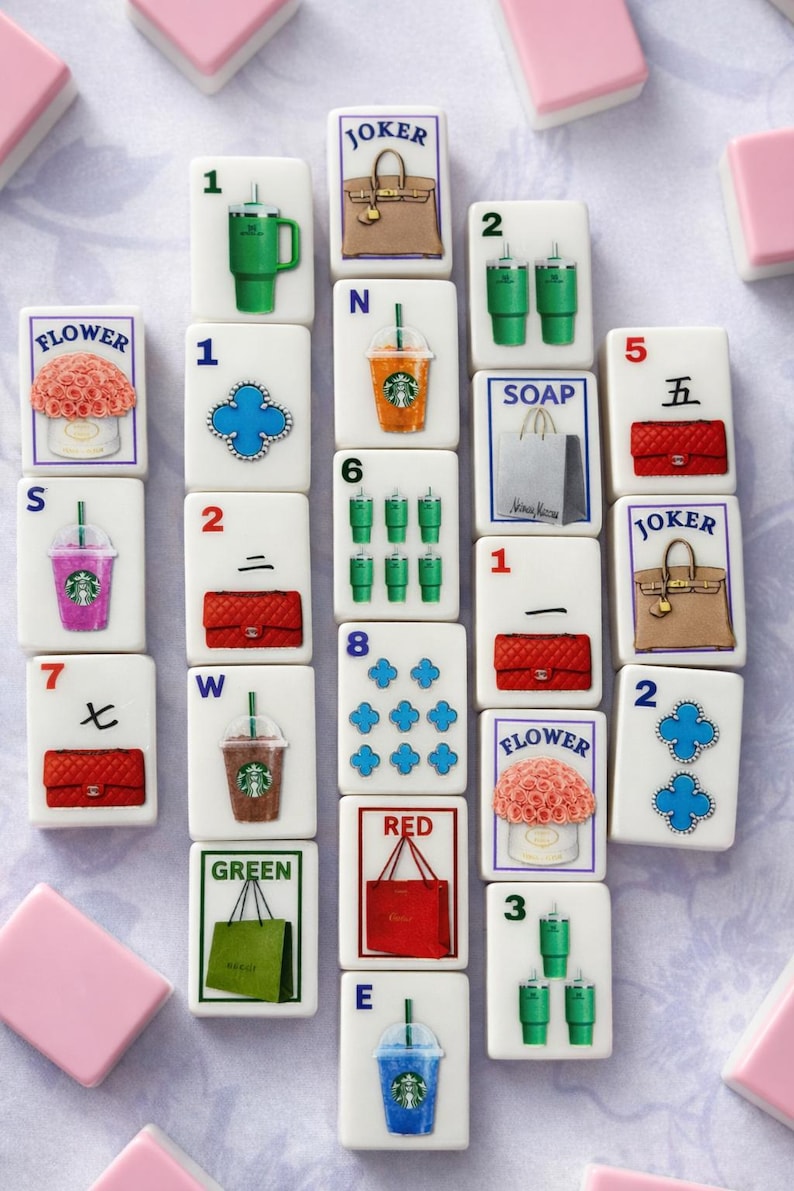 Puede incluir: Un conjunto de fichas de Mahjong blancas con varias ilustraciones, incluyendo bolsos, flores y bebidas. Las fichas presentan n&uacute;meros, letras y s&iacute;mbolos, con fichas rectangulares rosas y blancas.