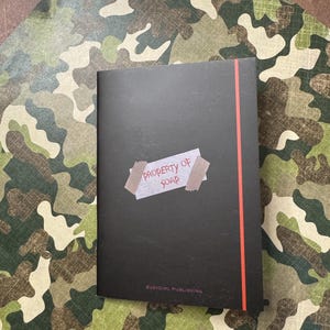 May include: A black notebook with a red stripe down the side. The notebook has a white label with the text "PROPERTY OF SOAP" on it. The notebook also has the text "BABY GIRL PUBLISHING" on the bottom.