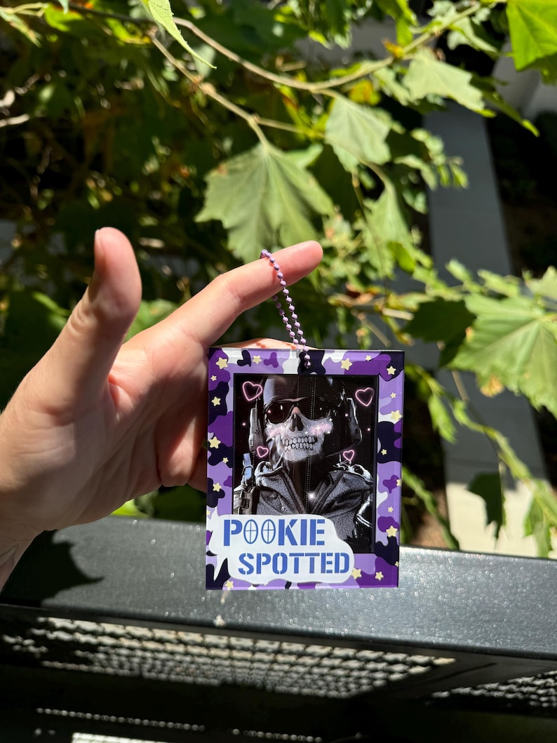May include: A purple and black keychain with a skull wearing sunglasses and a heart-shaped frame. The keychain has the text "POOKIE SPOTTED" on it.