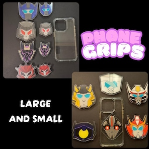 May include: A set of phone grips featuring Transformers characters. The grips are available in both large and small sizes. The grips are made of clear plastic and feature a variety of characters, including Optimus Prime, Megatron, and Bumblebee. The grips are designed to be attached to the back of a phone case.
