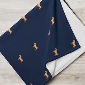May include: A navy blue fleece blanket with a repeating pattern of brown horses standing on their hind legs. The blanket is folded in half, showing the white fleece backing.
