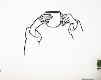 May include: Black metal wall art featuring a stylised outline of a person holding a coffee cup. The art is mounted on a white wall above a wooden cabinet with drawers.