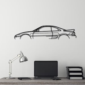 May include: A black metal silhouette of a sports car hangs on a white wall above a desk with a laptop, lamp, and a black stool.