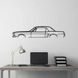 May include: A black metal outline of a classic car hangs on a white wall above a desk with a laptop, lamp, and a black stool.