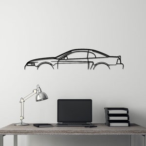 May include: A black metal outline of a car, mounted on a white wall above a desk with a lamp, a laptop, and a black chair.