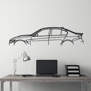 Op de afbeelding: Zwarte lijntekening van een auto op een witte muur. De auto is een sedan met een modern design. Een bureau met een laptop, lamp en kruk staan op de voorgrond.