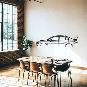 May include: A black metal car outline wall art. The car is a sedan with a spoiler. The art is mounted on a white wall in a room with a wooden table and chairs.