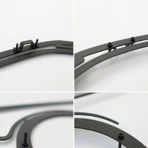 May include: Close-up of a black metal picture frame with various mounting hardware. The frame has a sleek, minimalist design with visible screws and a hanging bracket. The frame is designed to hold a picture or artwork.