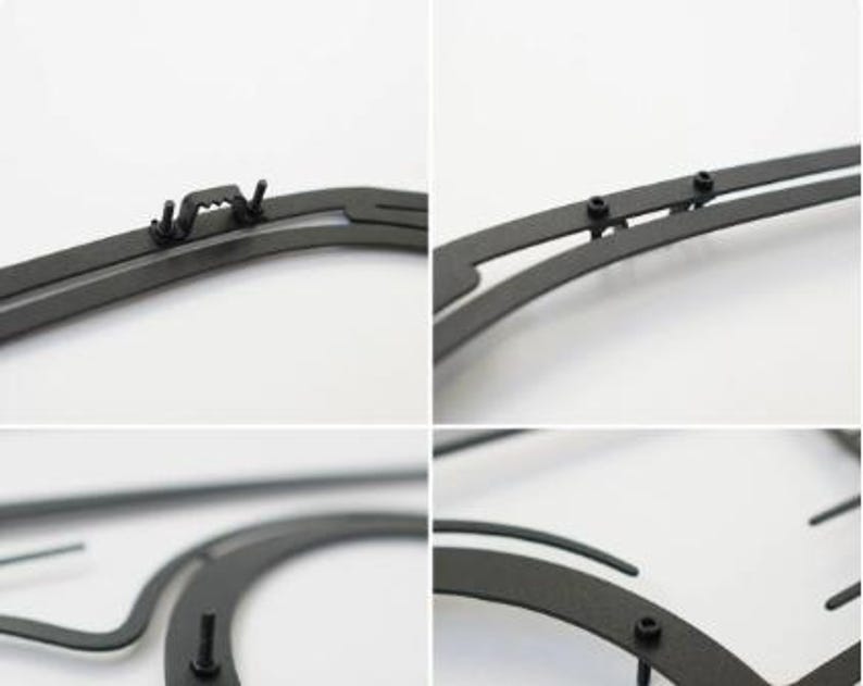May include: Close-up of a black metal picture frame with various mounting hardware. The frame has a sleek, minimalist design with visible screws and a hanging bracket. The frame is designed to hold a picture or artwork.