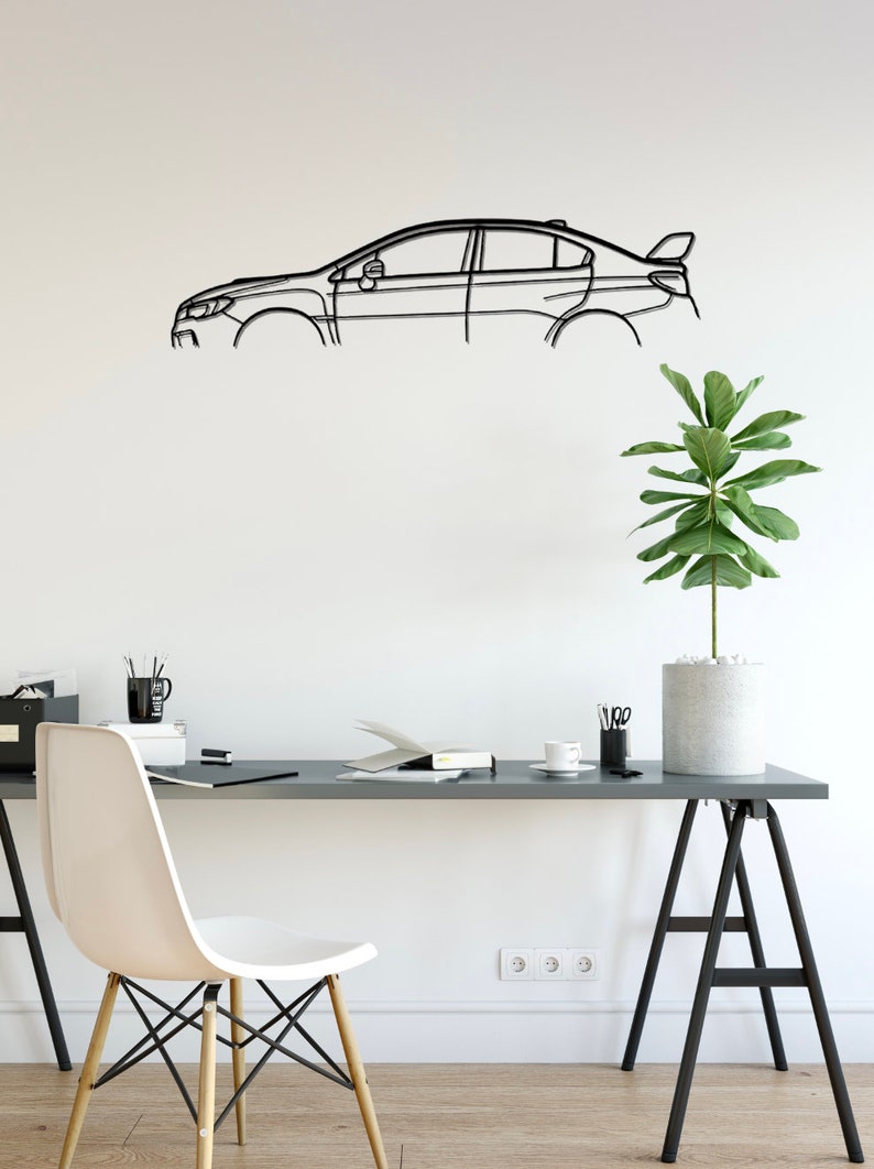 May include: A black metal car outline wall art. The artwork is mounted on a white wall above a desk. The desk has a white chair, a plant, and office supplies. The car outline is a modern, minimalist design.