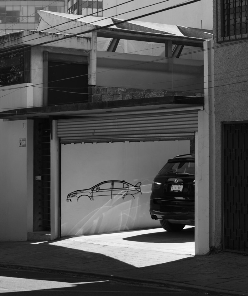May include: Monochrome image of a garage with a car inside. A car outline is drawn on the wall. The garage door is partially open, revealing the rear of a car. The building has a flat roof.