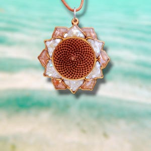 Op de afbeelding: Een houten hangerketting met een bloemmotief. De hanger heeft een centrale, getextureerde, bruine cirkel omgeven door witte en iriserende bloemblaadjes. De hanger hangt aan een bruin leren koord.