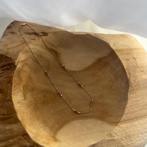 Könnte beinhalten: Eine zarte Goldkettenhalskette mit kleinen, gleichmäßig verteilten rosa Edelsteinperlen. Die dünne Metallkette hat einen Karabinerverschluss am Ende und ist in einer sanften Kurve angeordnet, die den Kontrast zwischen dem metallischen Gold und den rosa Akzenten betont.
