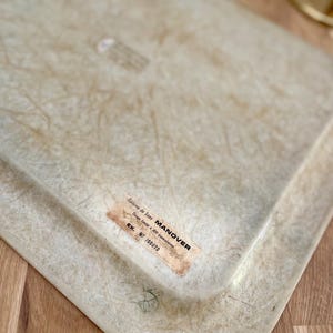 May include: A white, rectangular tray with a textured surface. The tray has a label that reads "Editions de Luxe MANOVER Trays Email & 600 Decorations EX. NF 100370".
