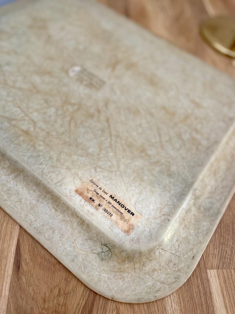 May include: A white, rectangular tray with a textured surface. The tray has a label that reads "Editions de Luxe MANOVER Trays Email & 600 Decorations EX. NF 100370".