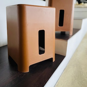 Puede incluir: Dos taburetes de plástico marrón con forma rectangular y un recorte en la parte delantera. Los taburetes están en un conjunto de escaleras con un suelo de madera oscura.