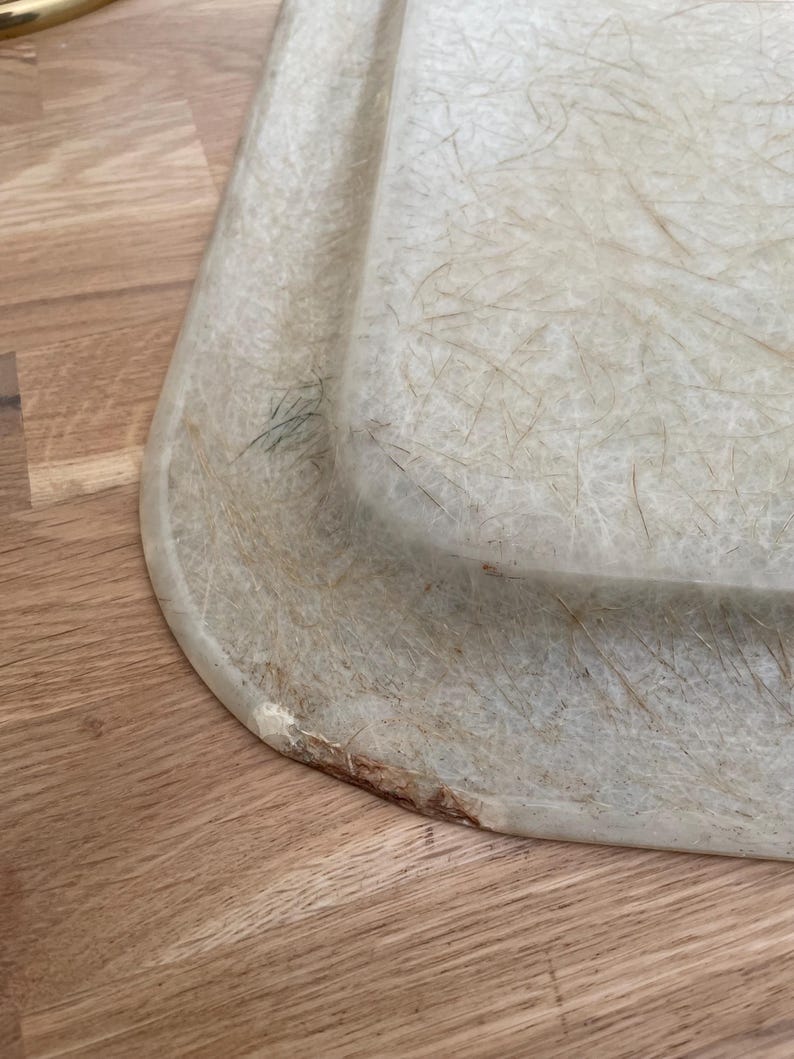 May include: A close-up of a light green, rectangular,  tray made of a material that resembles fiberglass. The tray has a slightly rounded edge and shows signs of wear and tear.