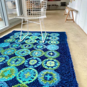 May include: A blue shag rug with a pattern of green and blue circles. A white wire chair sits on the rug.