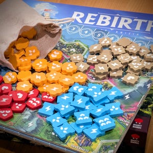 May include: A board game titled Rebirth featuring a game board with map illustrations, a beige fabric drawstring bag, and numerous small, shaped wooden tokens in orange, red, blue, and tan colors, some marked with white lightning bolt symbols.