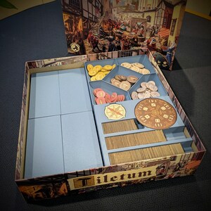 Peut inclure: Une bo&icirc;te de jeu de soci&eacute;t&eacute; Tiletum avec un organisateur interne contenant des piles de cartes, divers jetons circulaires color&eacute;s, un marqueur rond style boussole et un plateau circulaire pour d&eacute;s avec les chiffres un &agrave; six imprim&eacute;s.