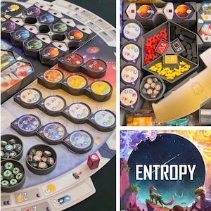 May include: A board game titled Entropy featuring a game board with circular planet tiles, gray plastic resource trays, and small tokens. The game includes a central hexagonal organizer filled with red, yellow, and black resource pieces and circular markers.