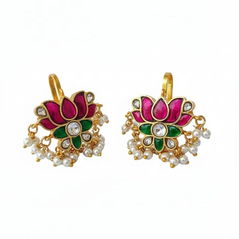 May include: A pair of gold-colored earrings featuring a lotus flower design. The earrings have a magenta-colored flower with green accents and a central clear stone. Small white pearls dangle from the bottom of each earring.